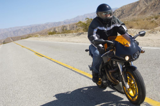 Motorcyclist wearing safety gear riding a motorcycle on a scenic highway, emphasizing motorcycle safety and awareness.