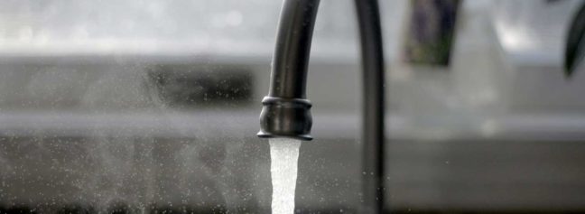 Water flowing from a black kitchen faucet, illustrating plumbing services and potential issues related to home plumbing disputes.