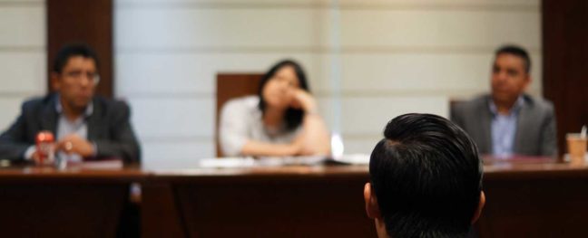 Person seated in front of three individuals in a legal setting, discussing personal injury settlements and legal representation.