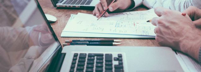 Hands reviewing legal documents on a desk with laptops, emphasizing collaboration and legal processes relevant to divorce and attorney fees in Virginia.
