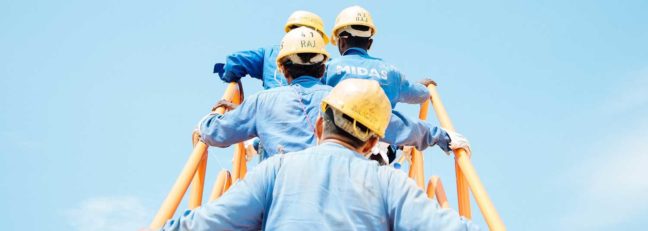 Construction workers in blue uniforms and hard hats ascending a ladder, symbolizing teamwork and the construction industry, relevant to legal guidance on construction contracts.