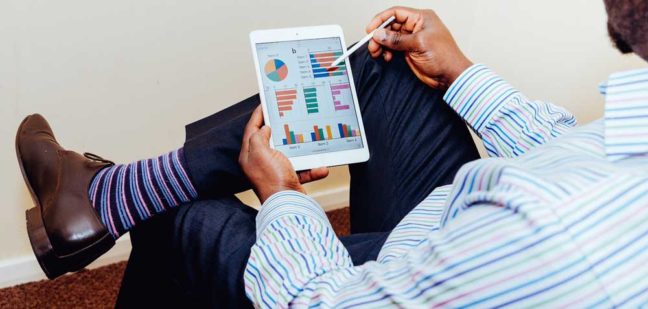 Person analyzing financial data on a tablet, wearing a striped shirt and dress shoes, representing legal and financial insights for divorce and asset protection.