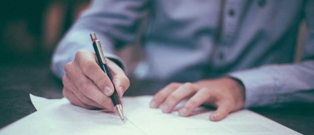 Person writing on legal documents, illustrating the process of divorce and financial considerations in family law.