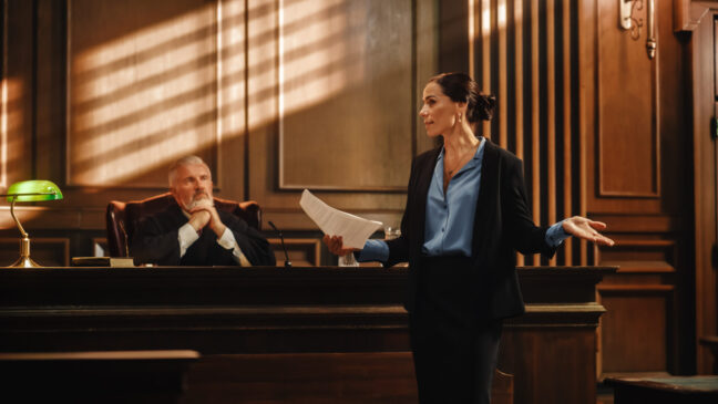 Female attorney presenting a case in a courtroom, with a judge observing, highlighting experienced trial representation in criminal defense.